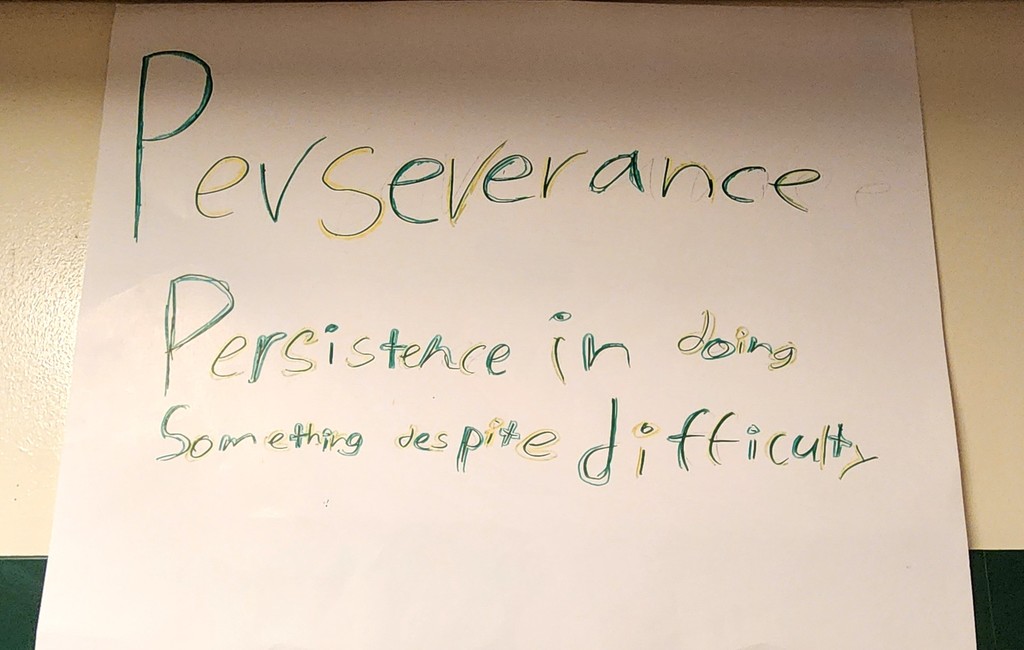 Handmade poster hanging on a wall with the word "Perseverance" drawn on it in green, blue and yellow with the caption "Persistence in doing something despite difficulty" underneath the word