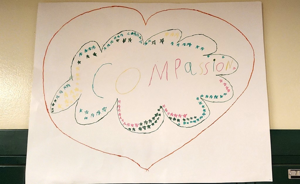 Handmade potster hanging on a wall with the word "Compassion" drawn inside a heart with colorful stars around the word.