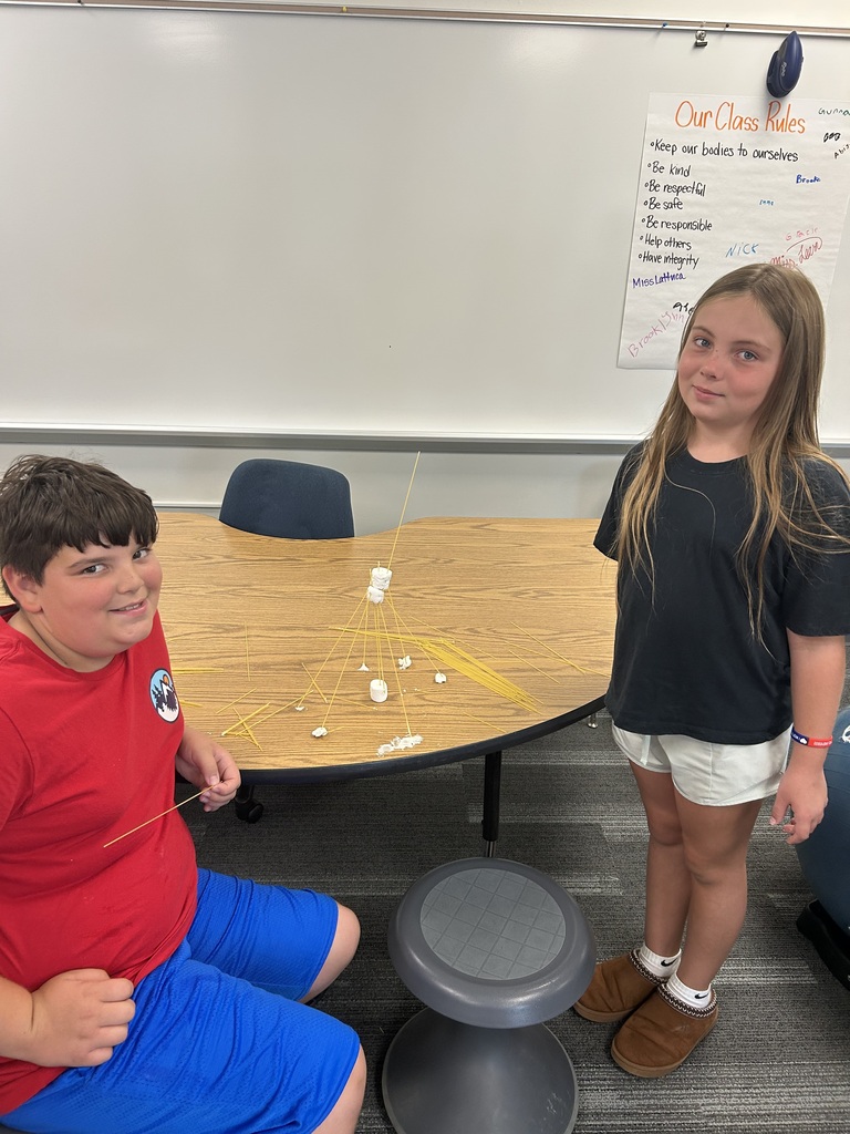 Students stand next to their towers made of spaghetti noodles and marshmellows