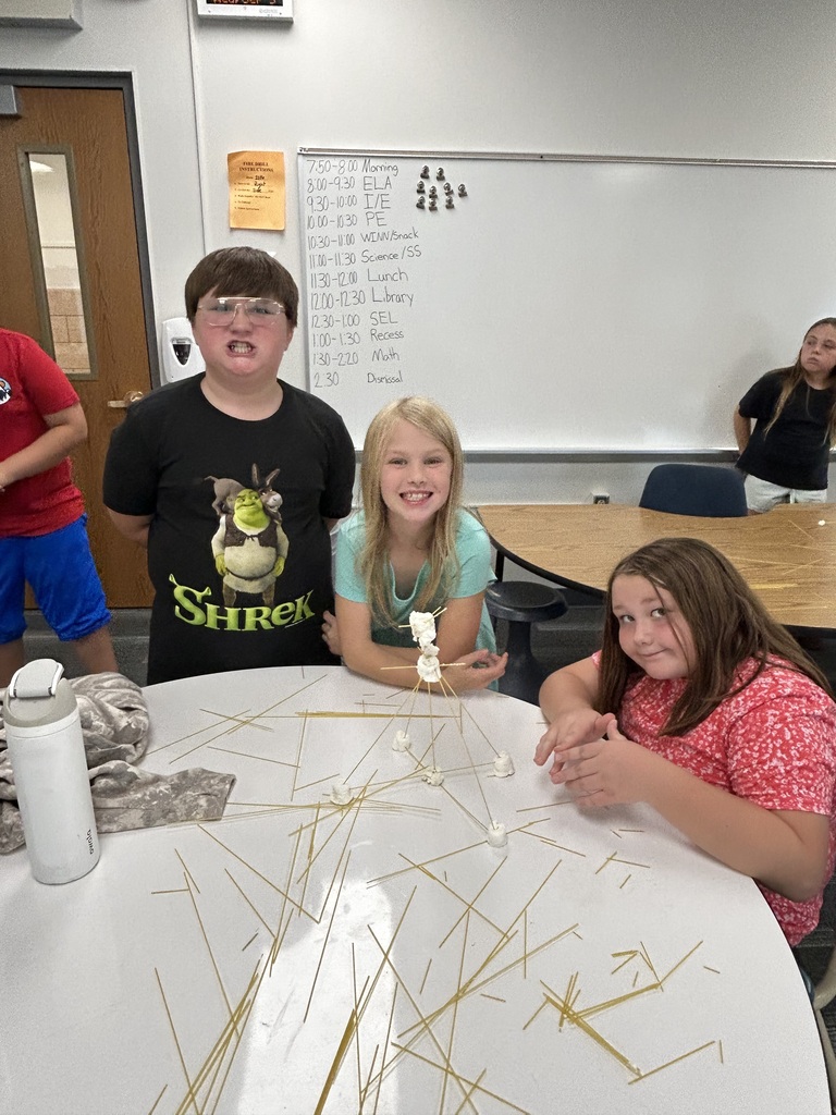 Students stand next to their towers made of spaghetti noodles and marshmellows