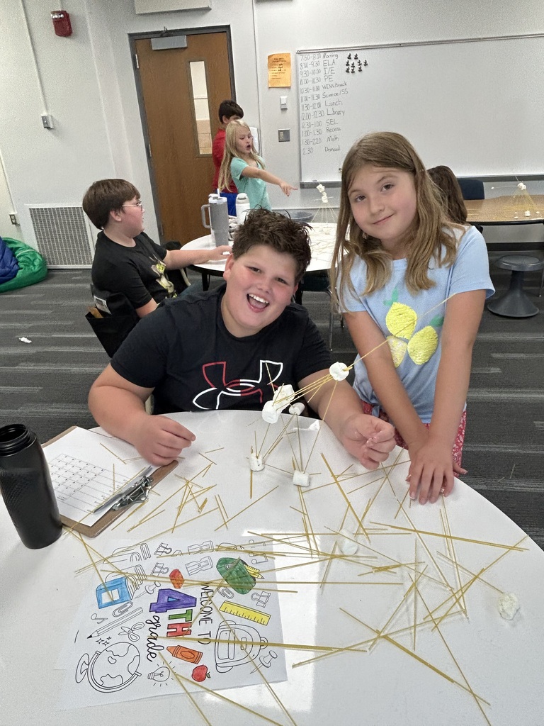 Students stand next to their towers made of spaghetti noodles and marshmellows