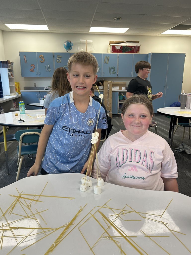 Students stand next to their towers made of spaghetti noodles and marshmellows