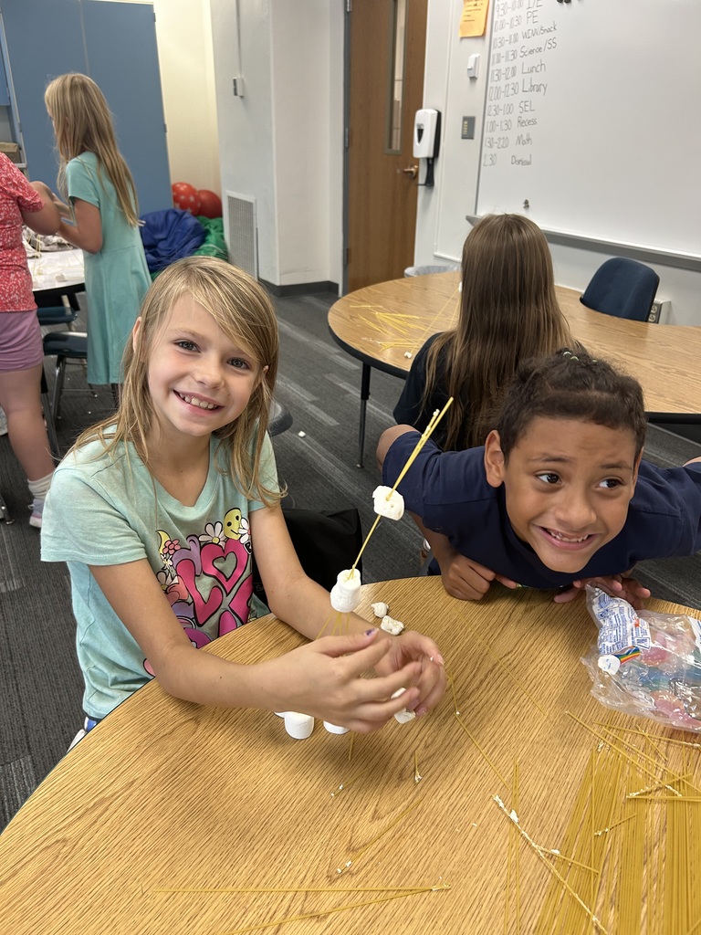 Students stand next to their towers made of spaghetti noodles and marshmellows
