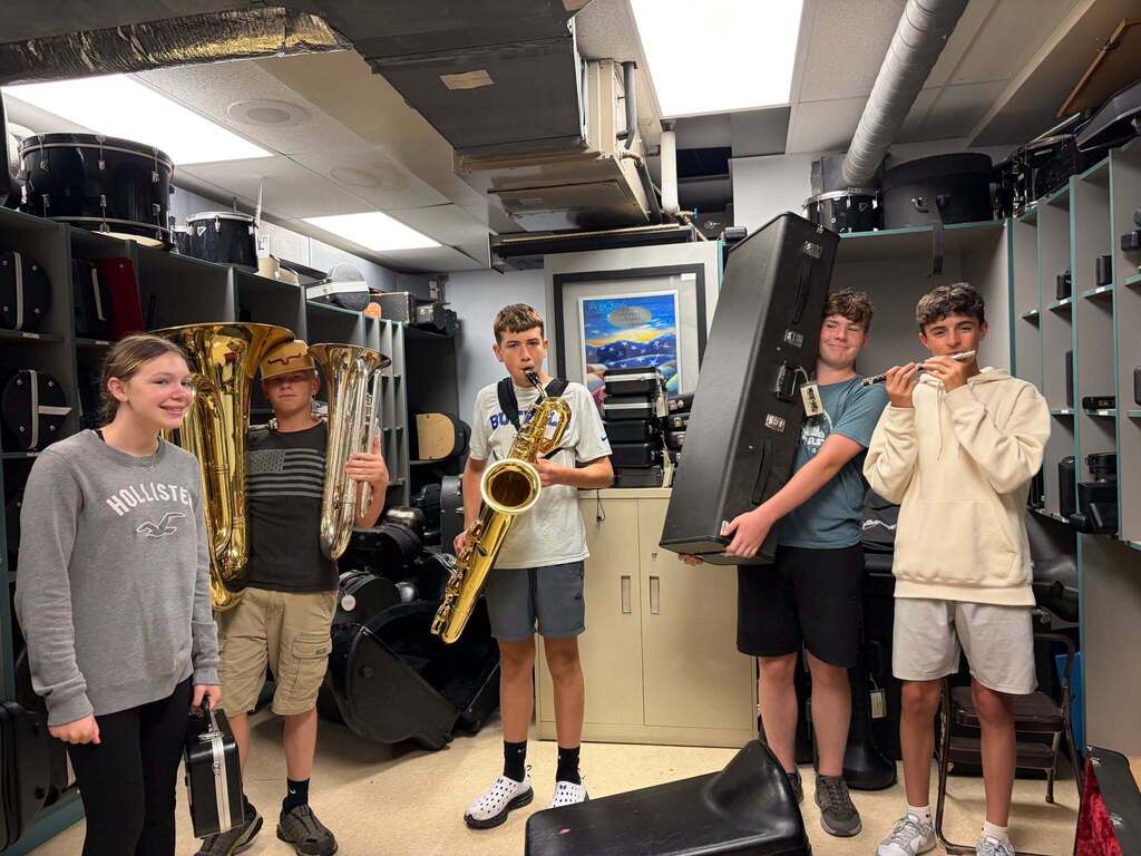 Students stand in the band storage room holding instruments