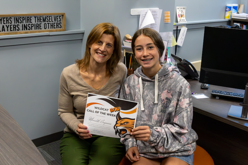 Student sits with Mrs. Kyle and holds certificate. 