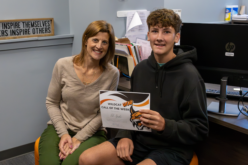 Student sits with Mrs. Kyle and holds certificate. 