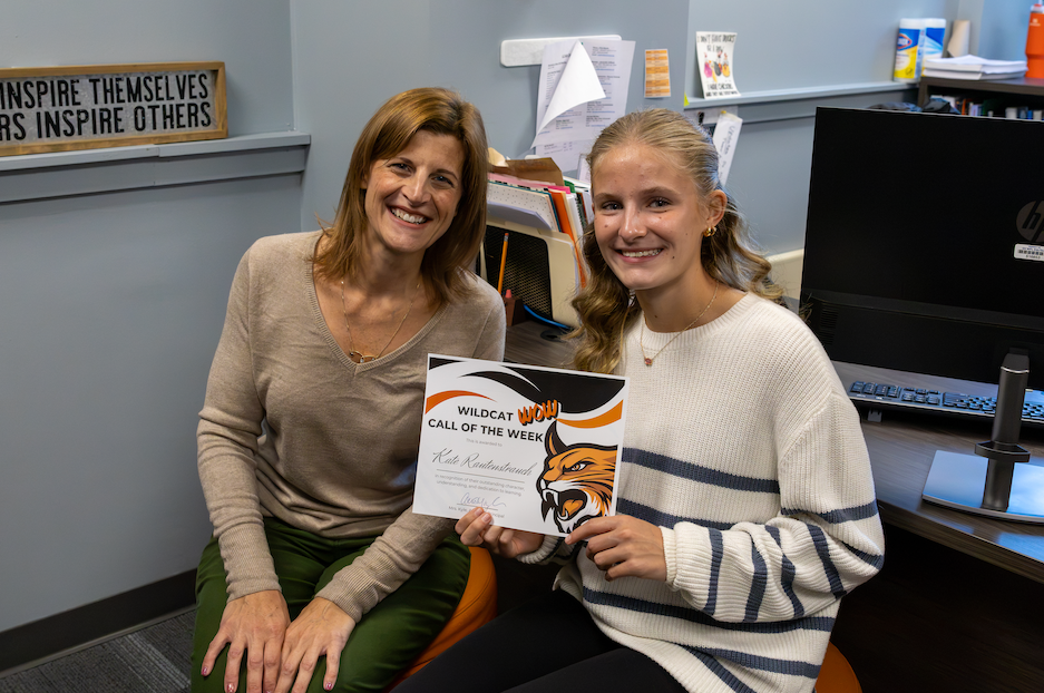 Student sits with Mrs. Kyle and holds certificate. 