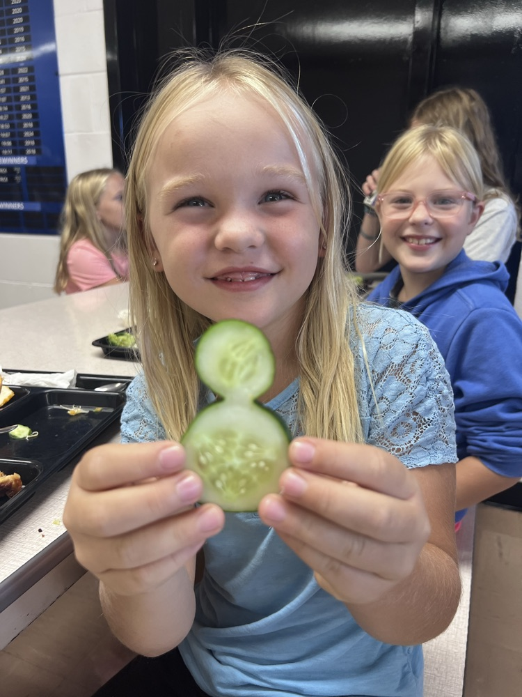 A girl holding a cucumber shaped like a snowman