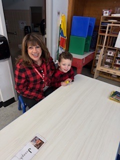 Teacher and student sitting at a table smiling, wearing the same shirt.