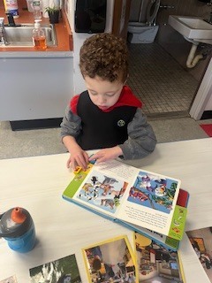 Pre K Student sitting at a table looking at a book.