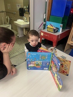 Pre K Student reading a book with a teacher