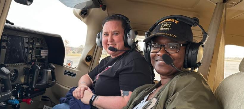 two women in a plane with their headgear on smiling at the camera