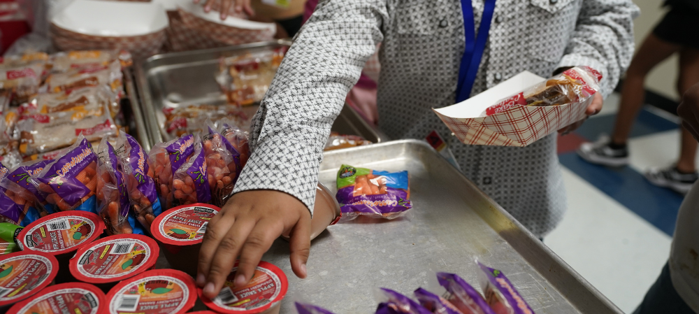 photo of a student grabbing an applesauce and holding a boat of food in his hand 