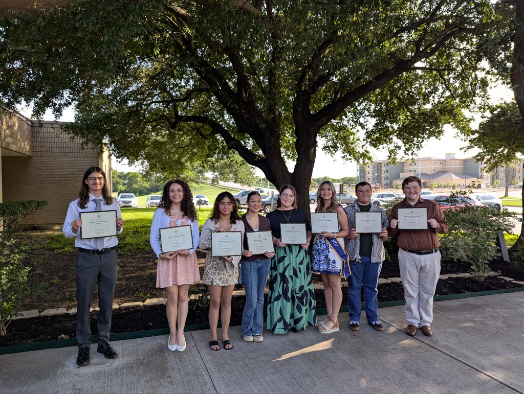 Eight student award winners holding certificates standing in front of a tree.