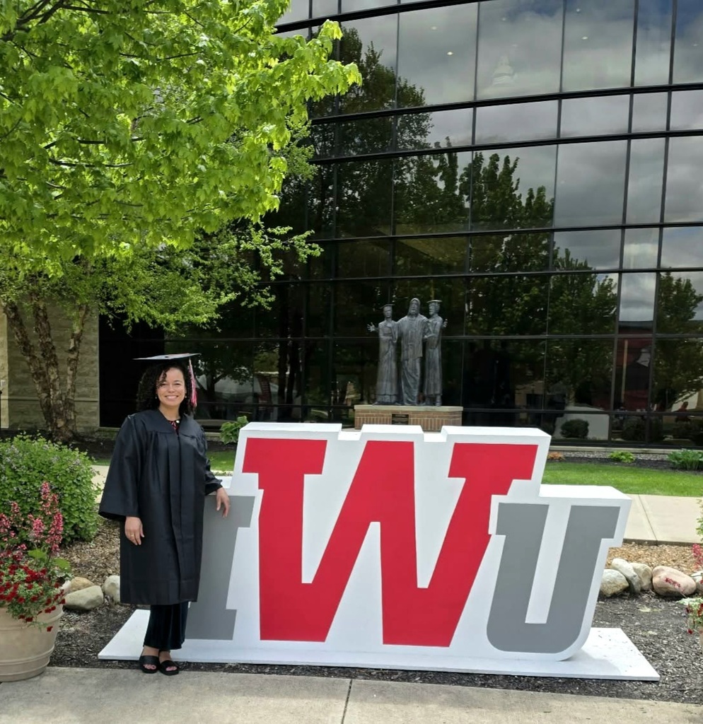 woman smiling at the camera next to a sign that says IWU