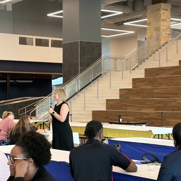 Teachers listen to a presenter in a cafeteria. 
