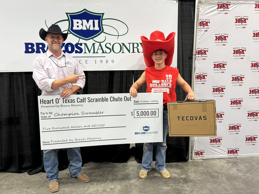 Two people stand next to each other holding a large check and a box. Behind them is a large banner with logos.
