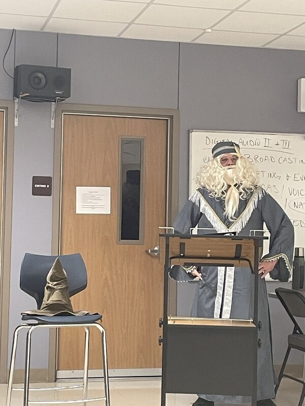 man with a wizard beard and uniform standing in front of a room with a  hat next to him