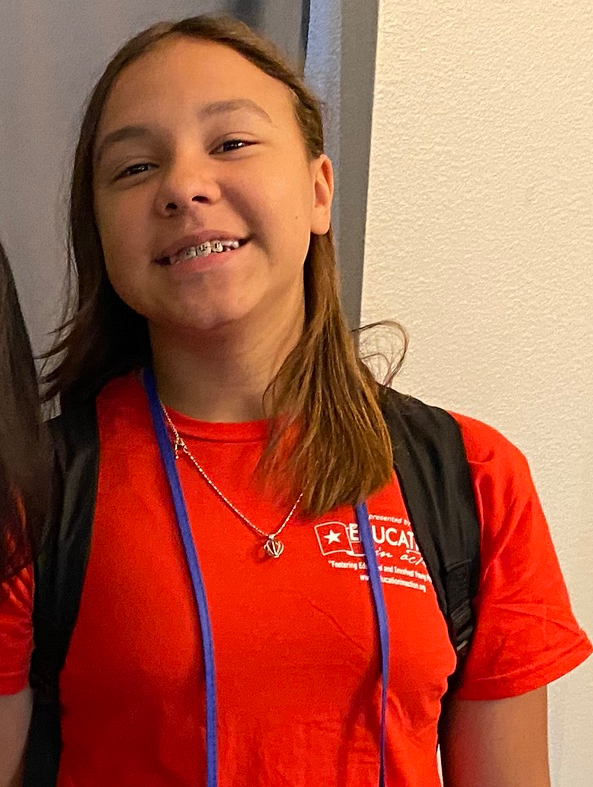 girl with brown hair and braces smiling at the camera wearing a red shirt