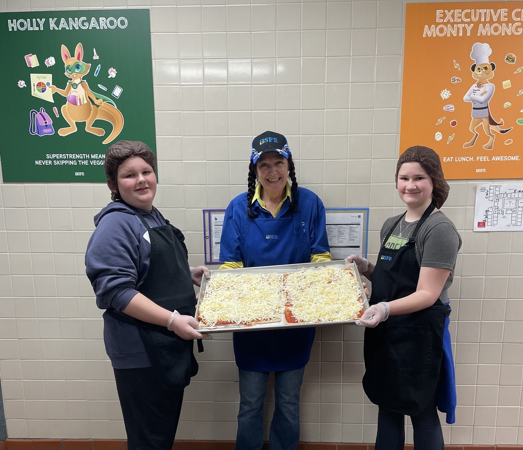 students holding pizza with kitchen staff