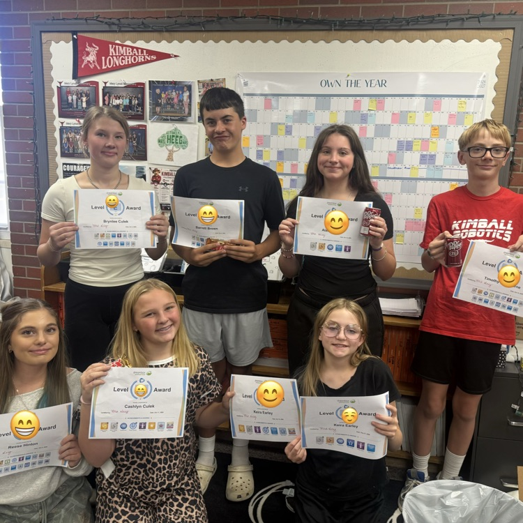 Several students pose with certificates and smiley faces while standing in a classroom.