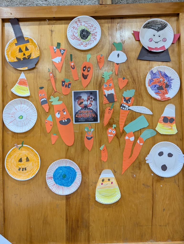Halloween crafts on a wall include paper plates with pumpkins, carrots, and faces. Some are decorated with candy corn and a Halloween movie poster.