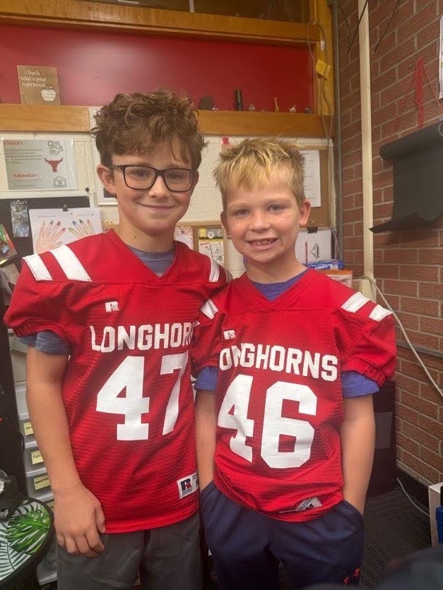 Two young boys in red football jerseys stand next to each other. One says 47, the other 46.