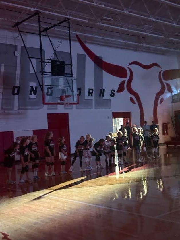 A group of young people stand in a gymnasium with a basketball hoop and a red bull logo on the wall.