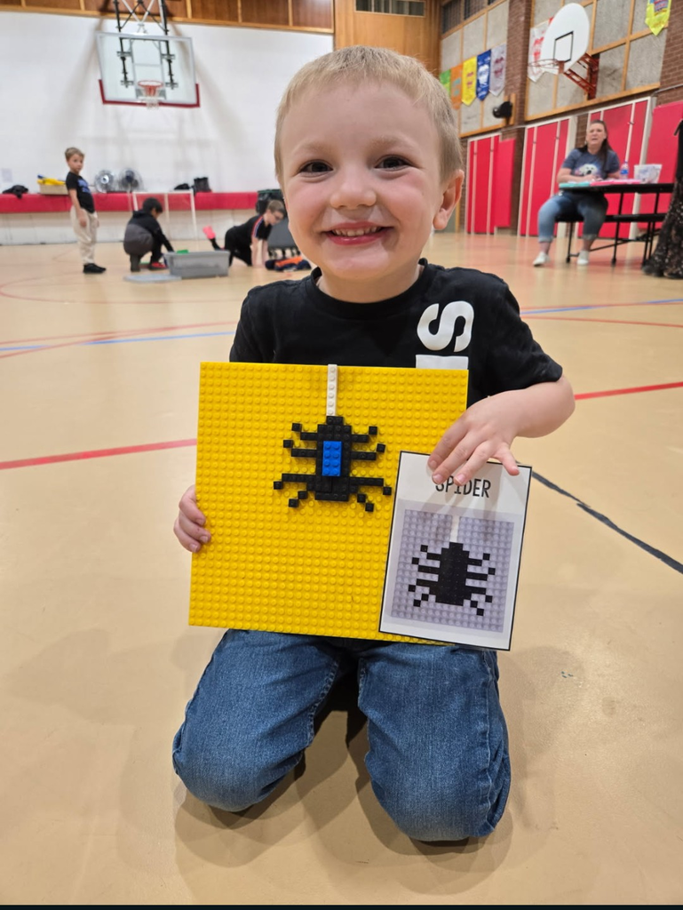 Child kneeling in gym holds yellow tile with a spider image and a sheet of paper.