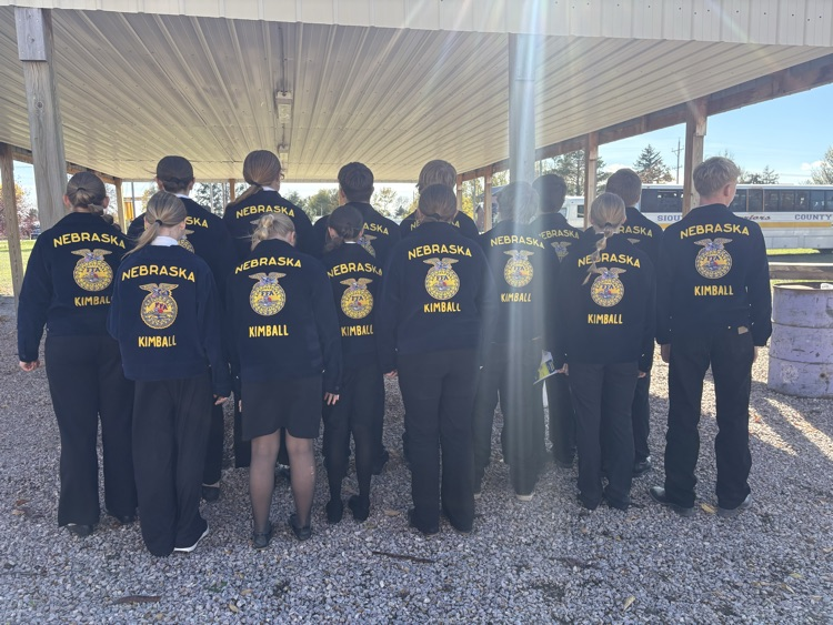 Group of students wearing matching uniforms lined up in a row with a bus in background.