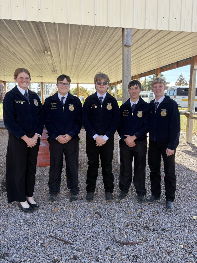 Five students in school uniforms stand outside under a canopy, next to a gravel area.