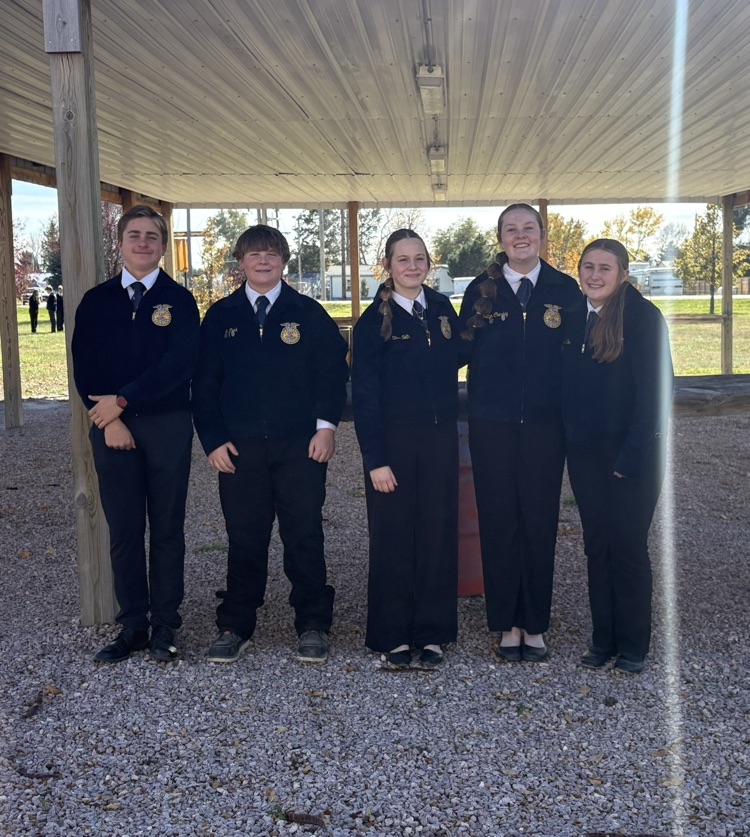 Five students in school uniforms stand together in a shed with a gravel floor.