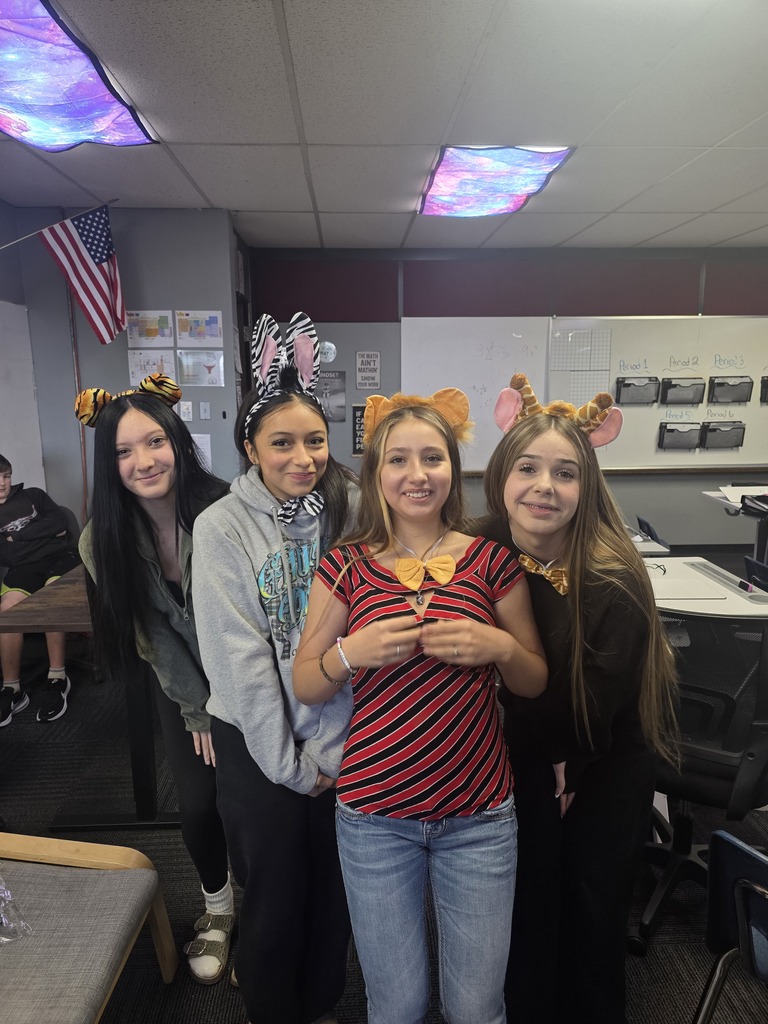 Four girls stand in a classroom, each with a set on animal ears on.