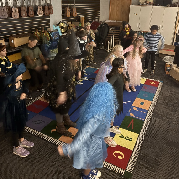 Several students in costumes stand on a colorful carpet, while guitars hang on the wall.