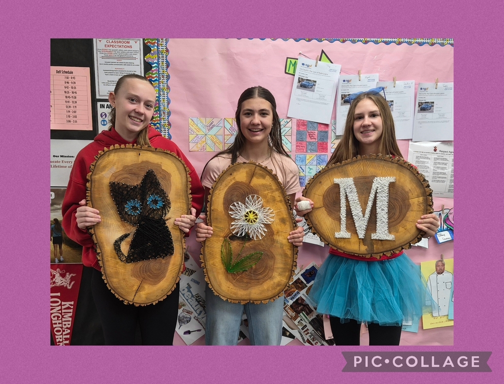 Three students hold wooden pieces with images and letters. Two pieces have cat and flower designs; one piece has letter M.