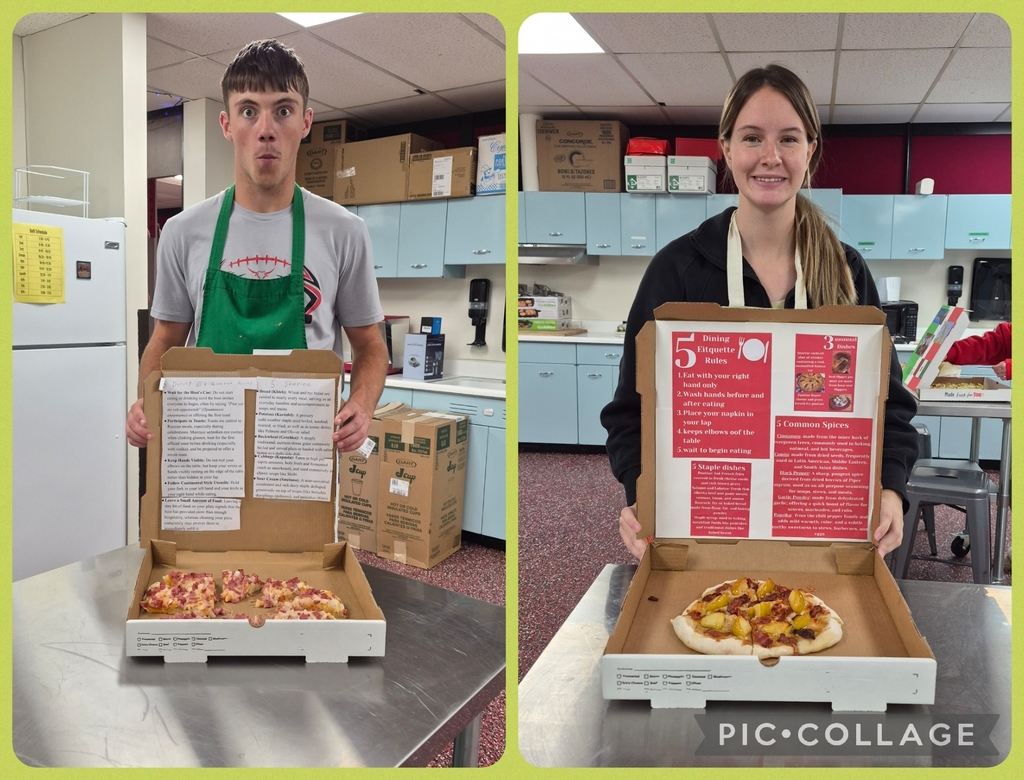 Two people hold open pizza boxes with pizza inside, on a countertop. Behind them, a kitchen with a refrigerator, cupboards, and boxes.