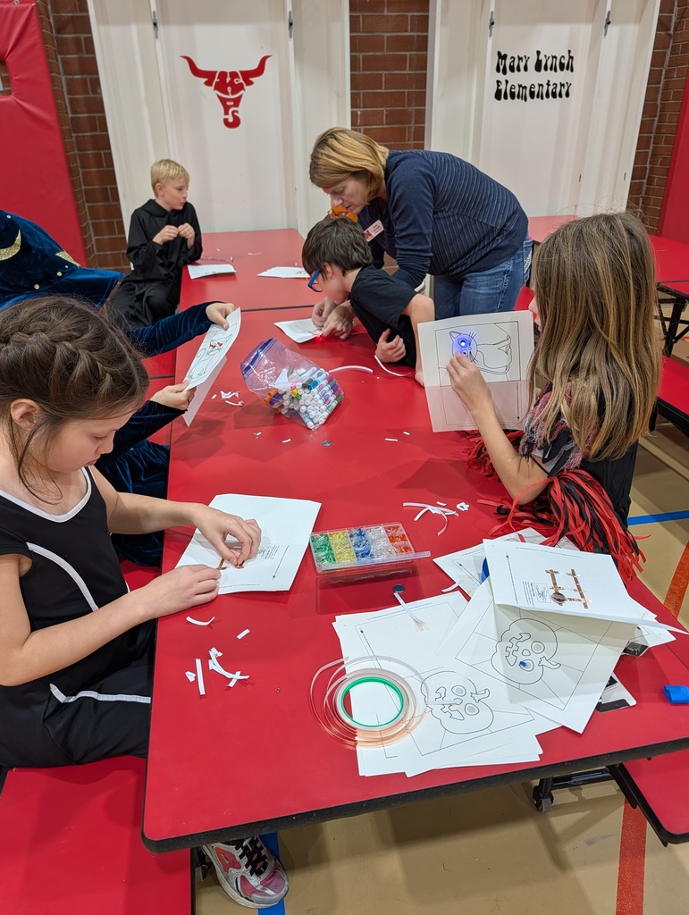 Four children and an adult woman seated around a red table, working on paper with markers.