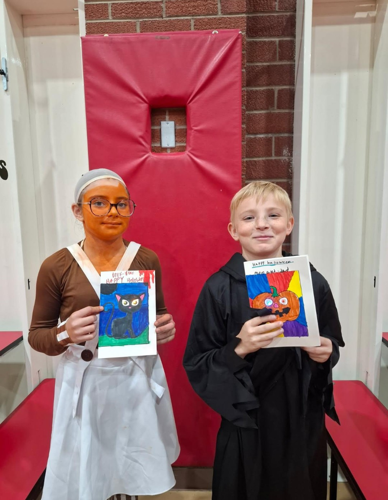 Two children standing; one holds a colorful drawing of a cat, the other a drawing of a witch.
