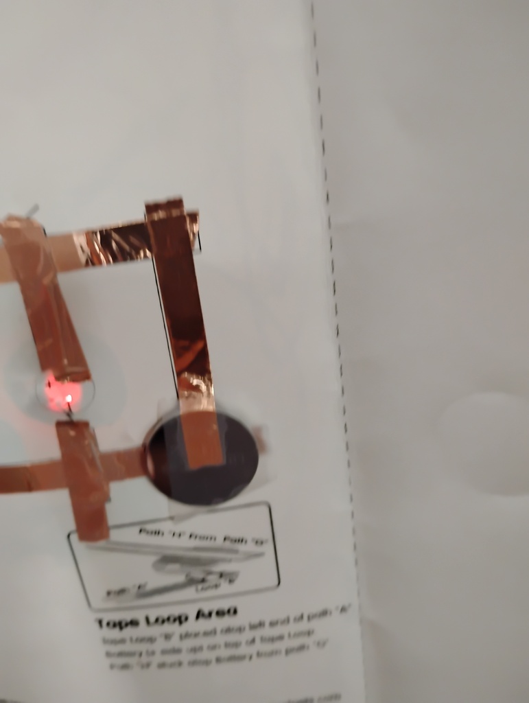 A close-up of a copper-colored circuit board with a light-up LED. A white background with a diagram is partially visible.