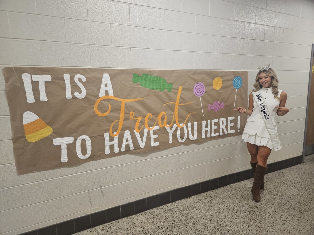 Miss Virginia in front of a bulletin board that says "It is a treat to have you here!"