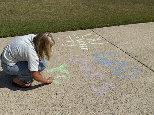 Students drawing positive messages on the sidewalk - You are worth it, God loves you