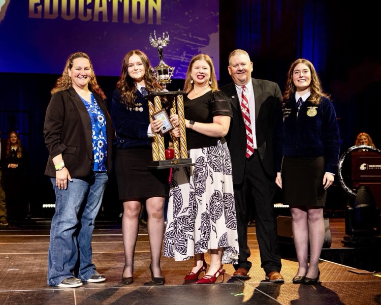 Lillianna on stage with trophy and others presenting with her 