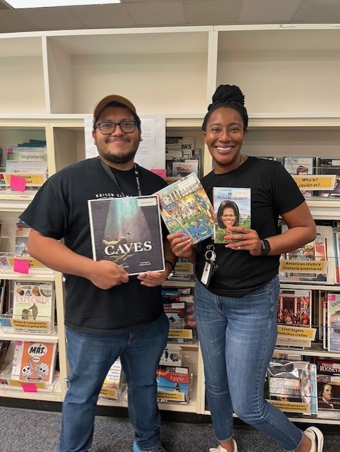 two smiling teachers holding books in the library