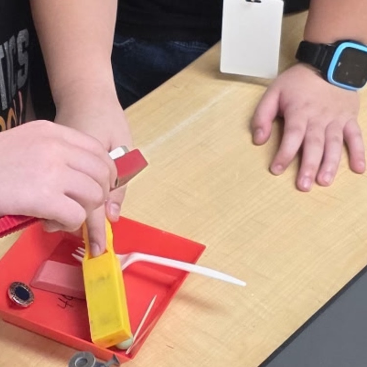 2 students with magnets and objects on red tray