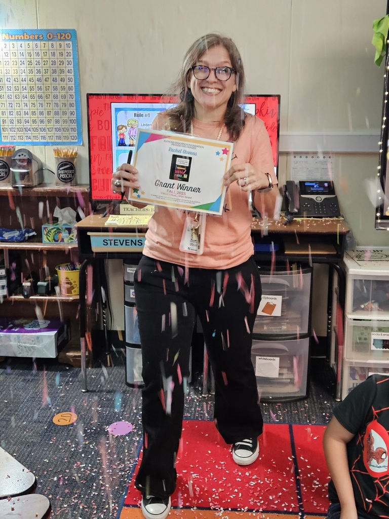 teacher smiling with confetti falling around her in a classroom