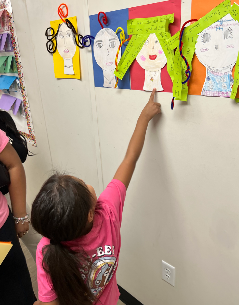Girl in pink shirt pointing at her classwork during Open House 