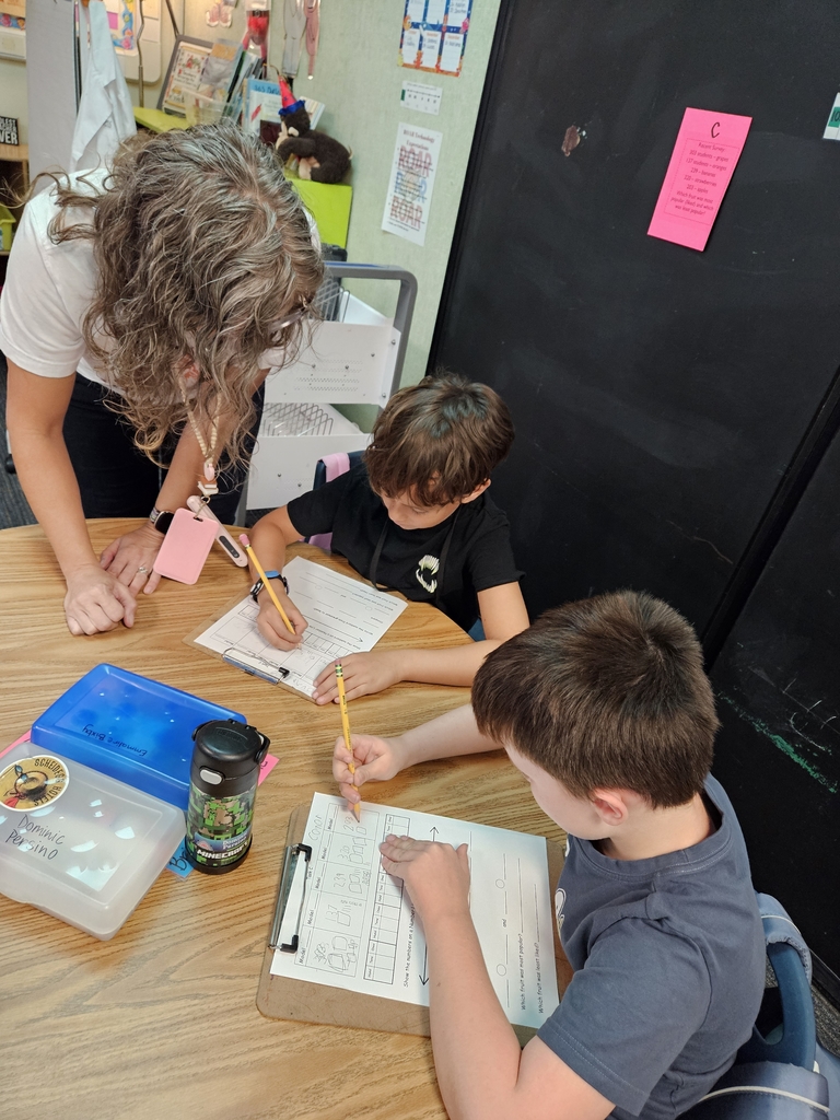 2 students working at a desk on math problem with teacher checking in with them