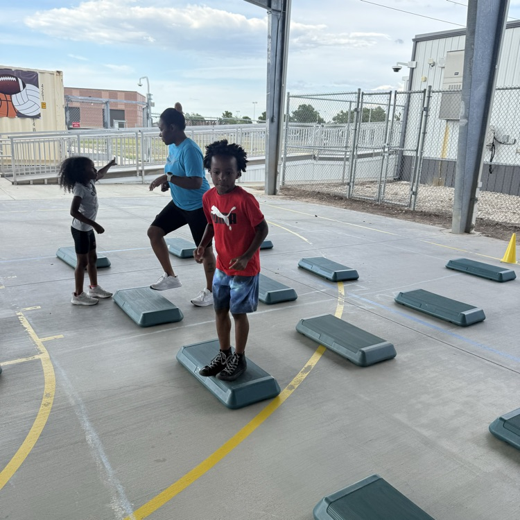 2 students in red and gray shirt with their mom in a blue shirt on steps for Zumba