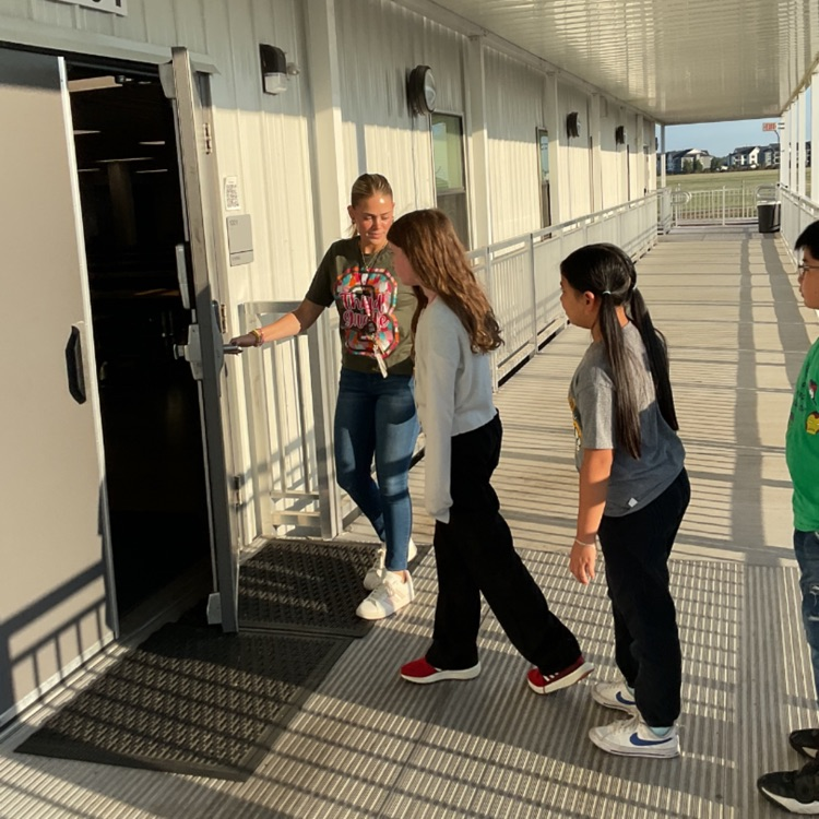 Resident in green shirt opening cafeteria door for 2 students
