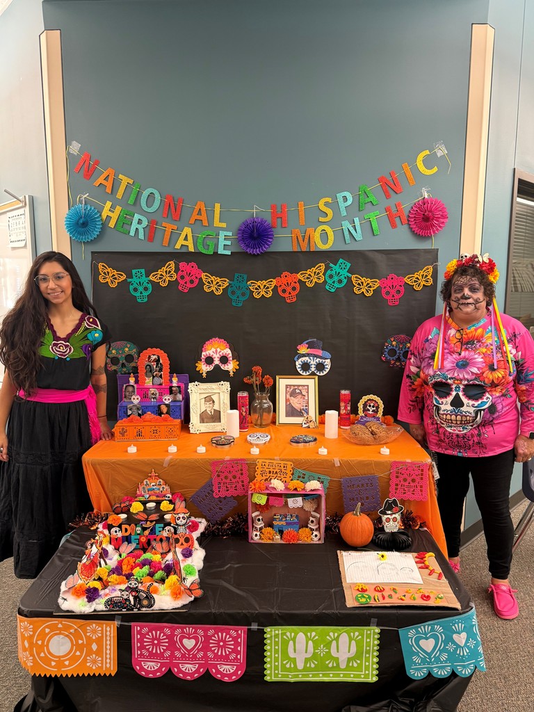 1st grade teachers pose next to display of Dia de los muertos altars